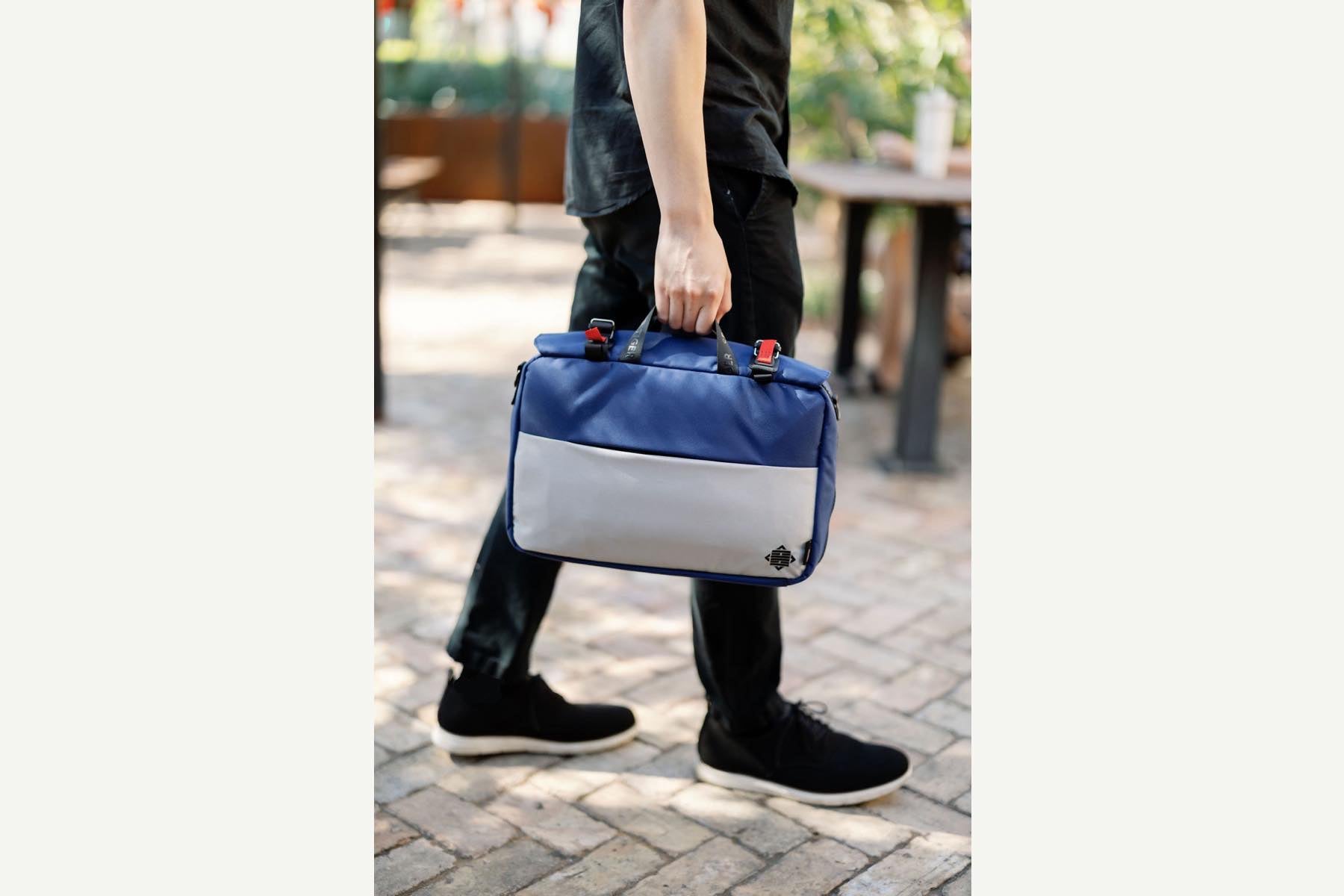 A male model holding the blue bag to show scale. The bag is 15" wide and 10" tall. 