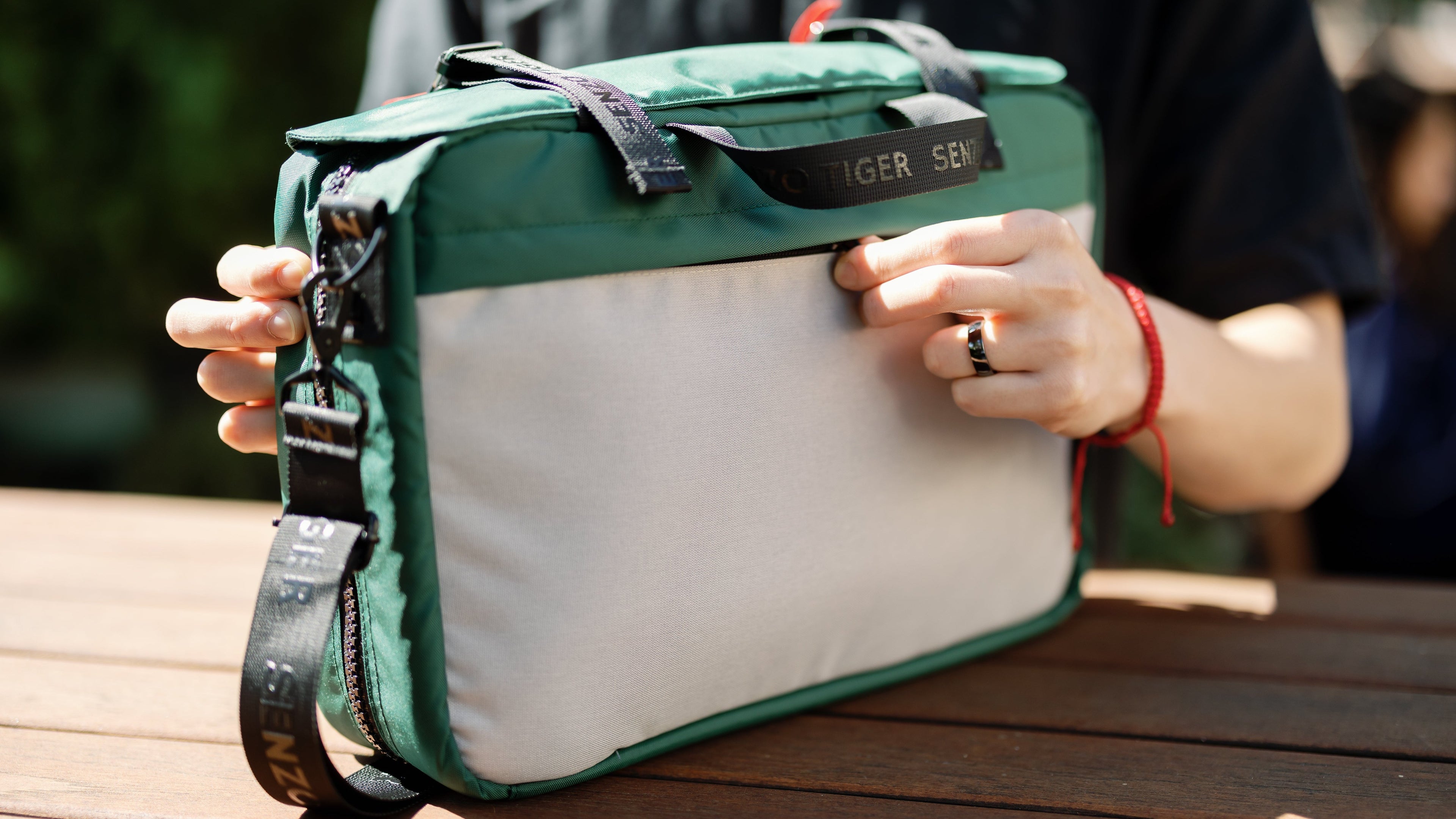 Man opening the back pocket of a green bag. 